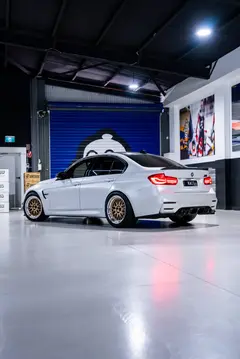 Alpine White BMW F80 M3 in motion featuring mesh-style Gold Volk Racing 21A wheels with shiny silver lips