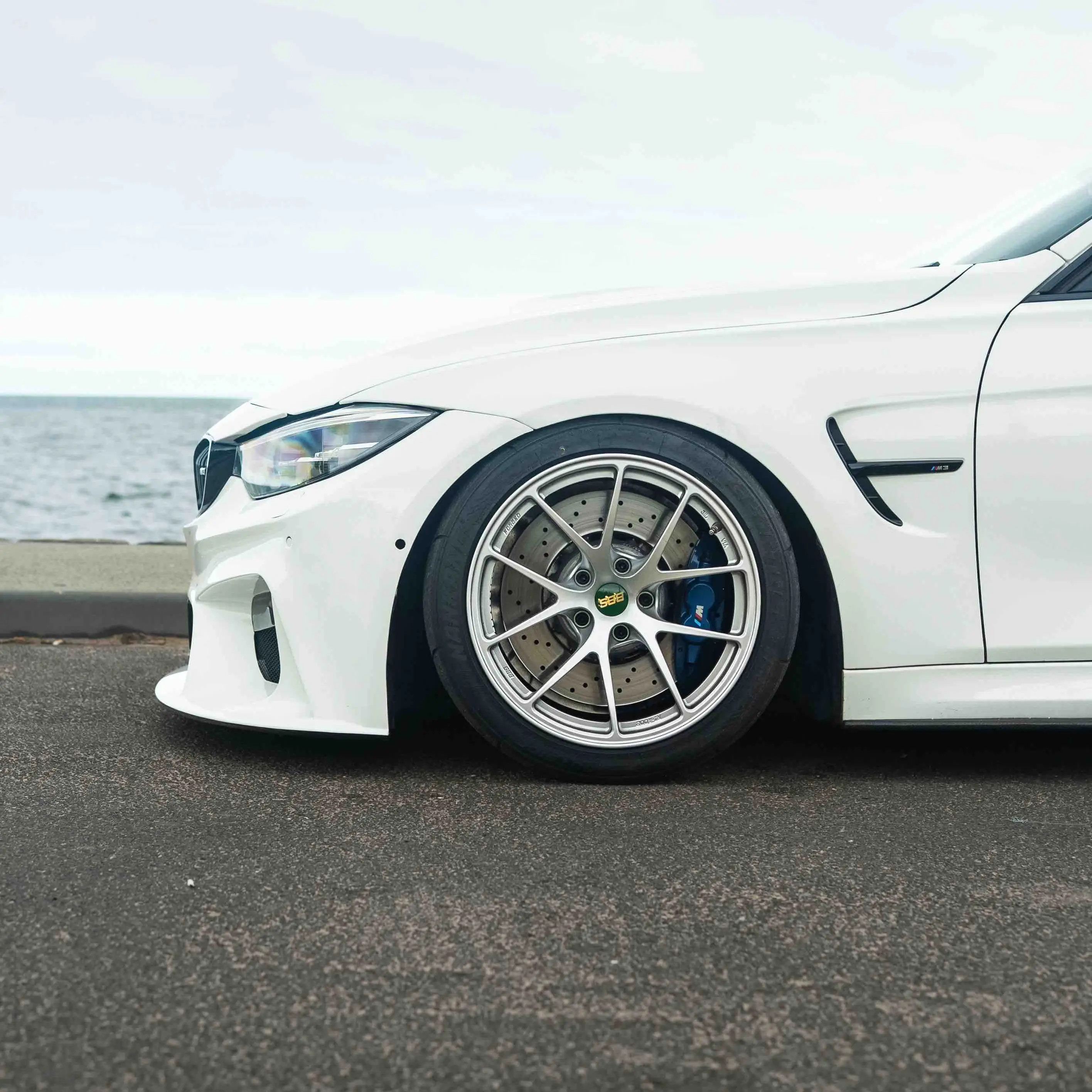 Low angle dynamic shot of a lowered white BMW M3 equipped with motorsport spec BBS RIA wheels
